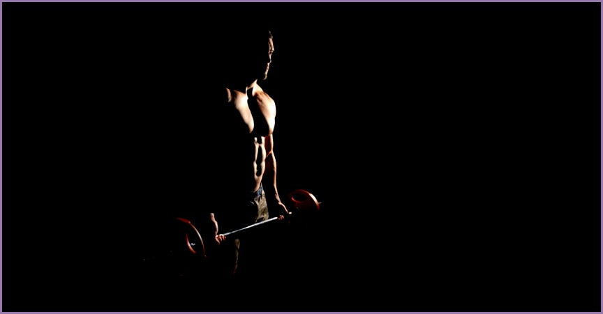 Muscular man training in gym lifting a barbell on black background 4K stock footage clip
